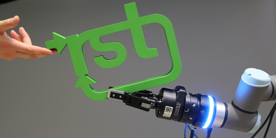 Roboterarm übergibt RST-Loga an Menschen