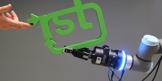 Roboterarm übergibt RST-Loga an Menschen