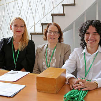 Zwei Frauen und ein Mann sitzen am Tisch der Teilnehmerregestrierung