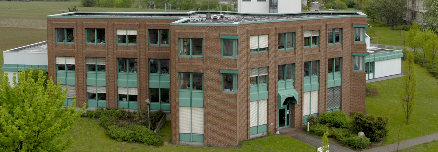 Institut für Roboterforschung: Ein Backsteingebäude mit türkisen Details an den Fenstern aus einer erhöhten Position fotografiert. Um das Gebäude herum Wiese. Im Hintergrund weitere Gebäude.